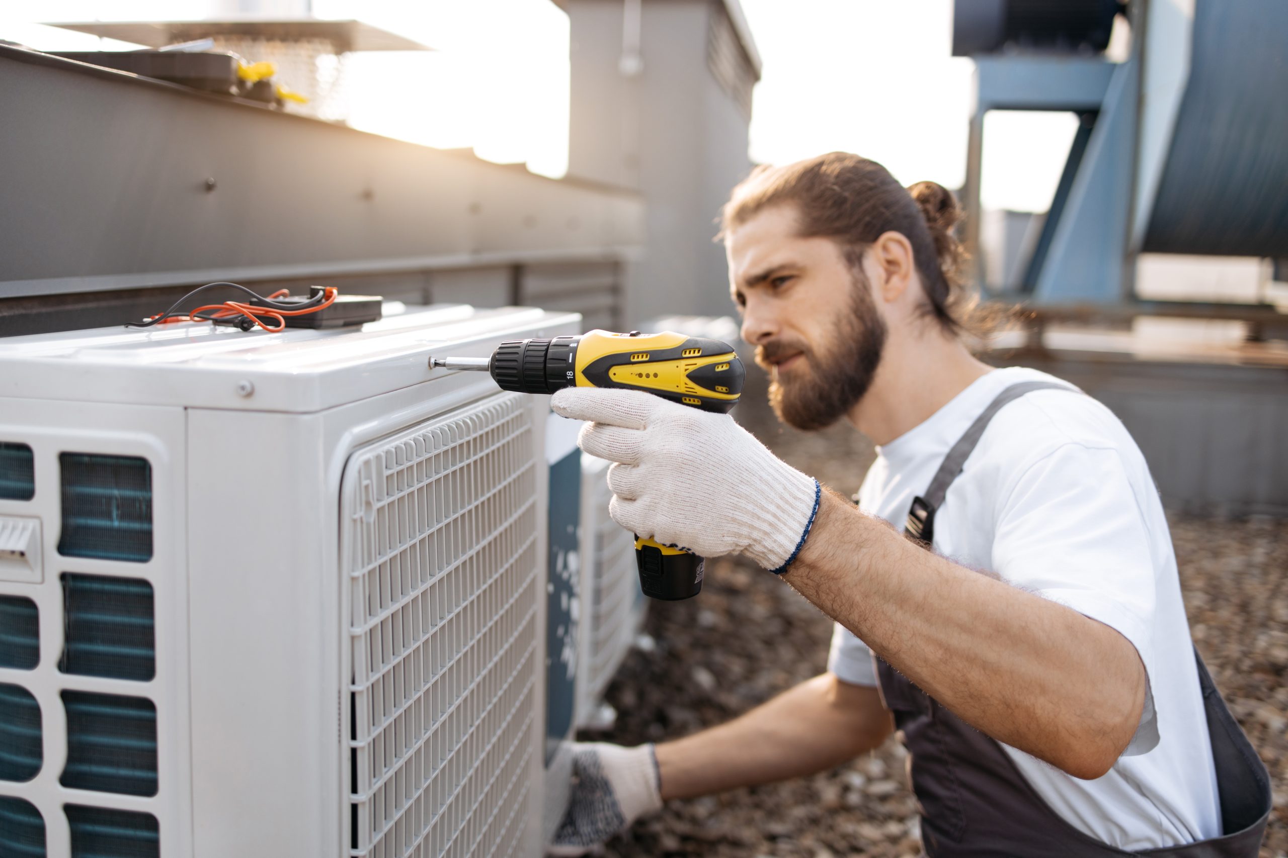 Male worker repairing conditioner while using drill outdoor